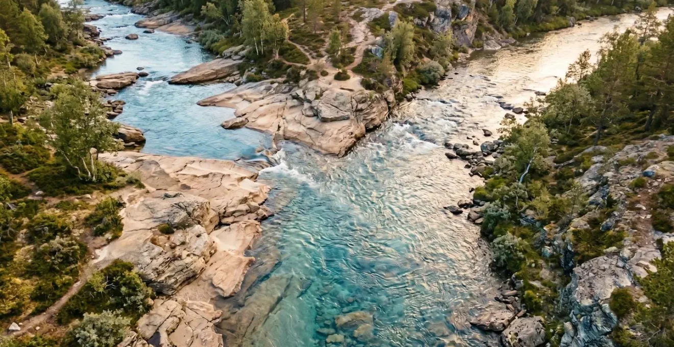 Vue aérienne de deux cours d'eau convergeant en une confluence harmonieuse, entourés de roches beiges claires et de végétation minimale, sous une lumière matinale dorée